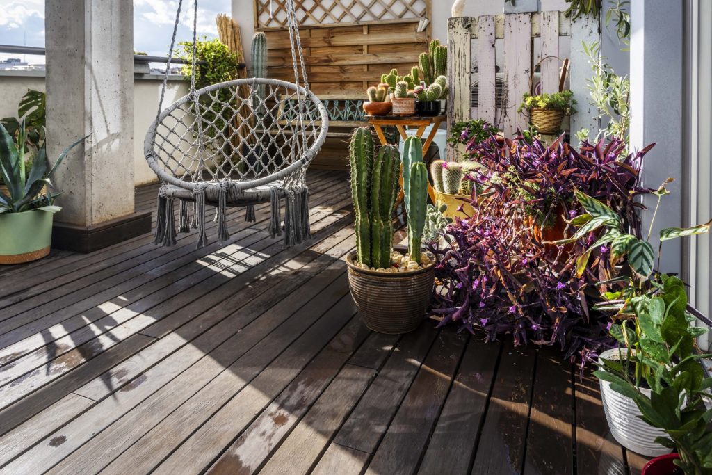 Ein Holzbalkon mit verschiedenen Topfpflanzen, Kakteen und einem hängenden Korbsessel.